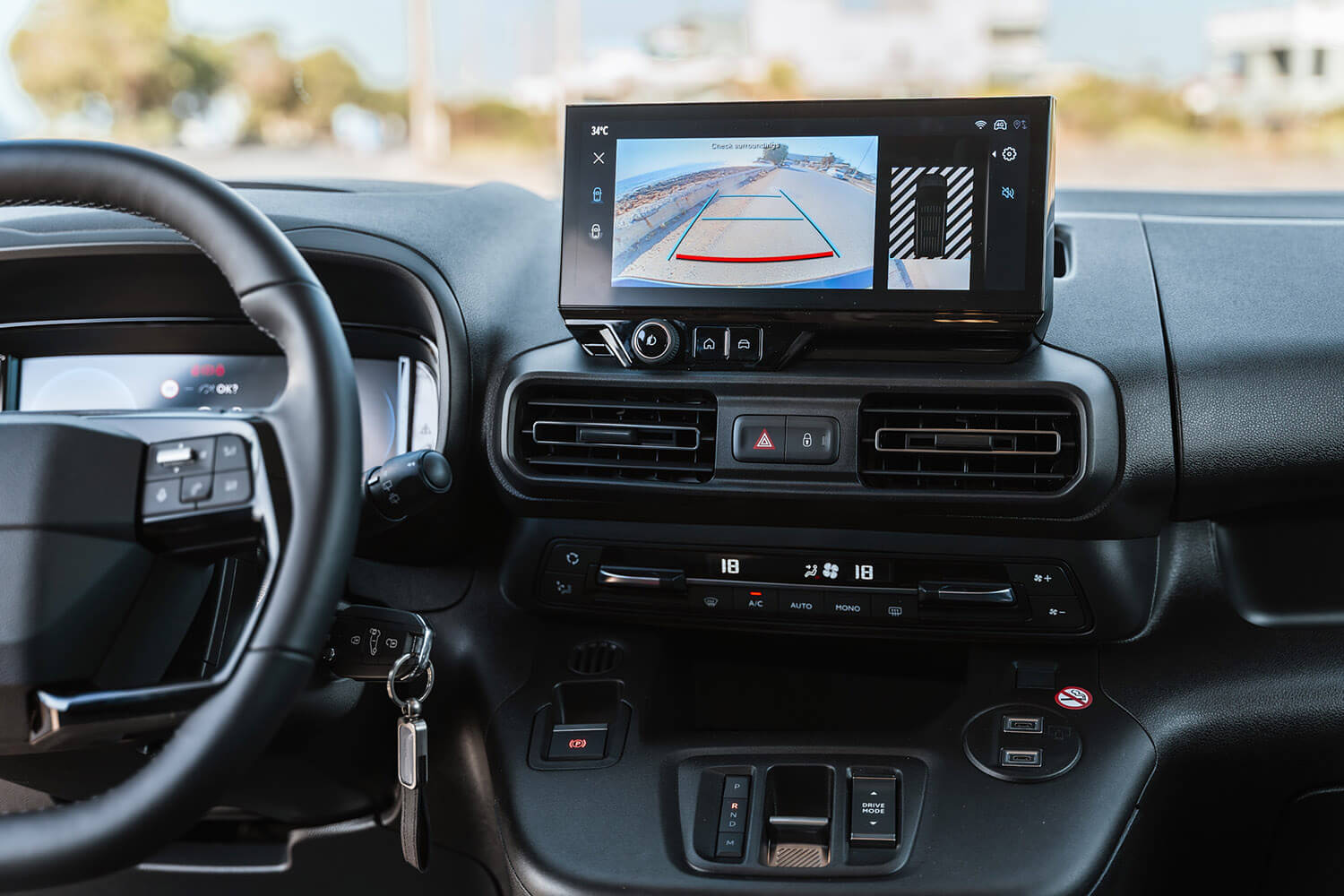Car interior showing a wide dashboard with a large touchscreen displaying a rearview camera feed and guidance lines behind the vehicle.