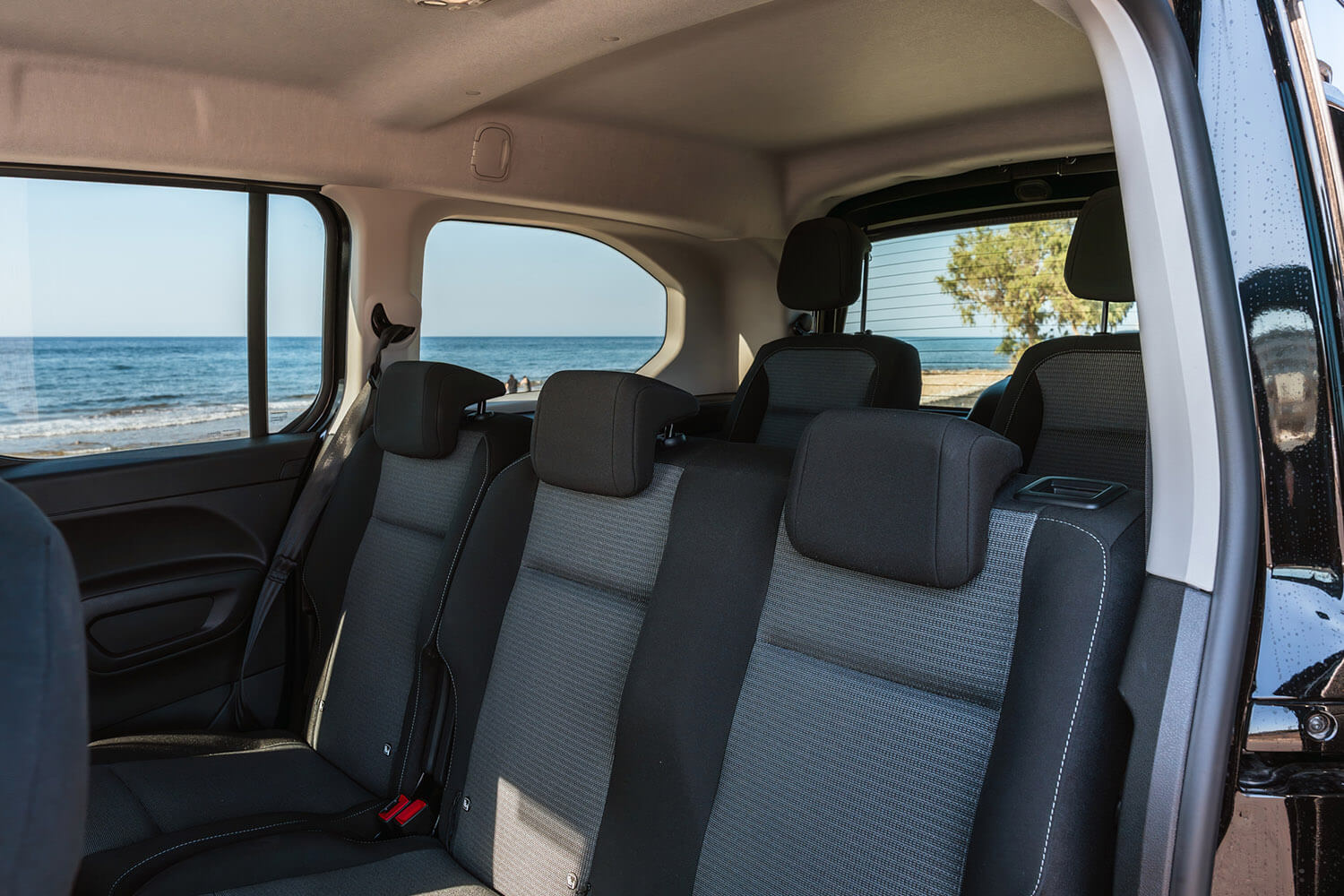 Back seat of a dark SUV with gray fabric, ocean visible through the side window. The beach is seen as the car is parked by the coast.