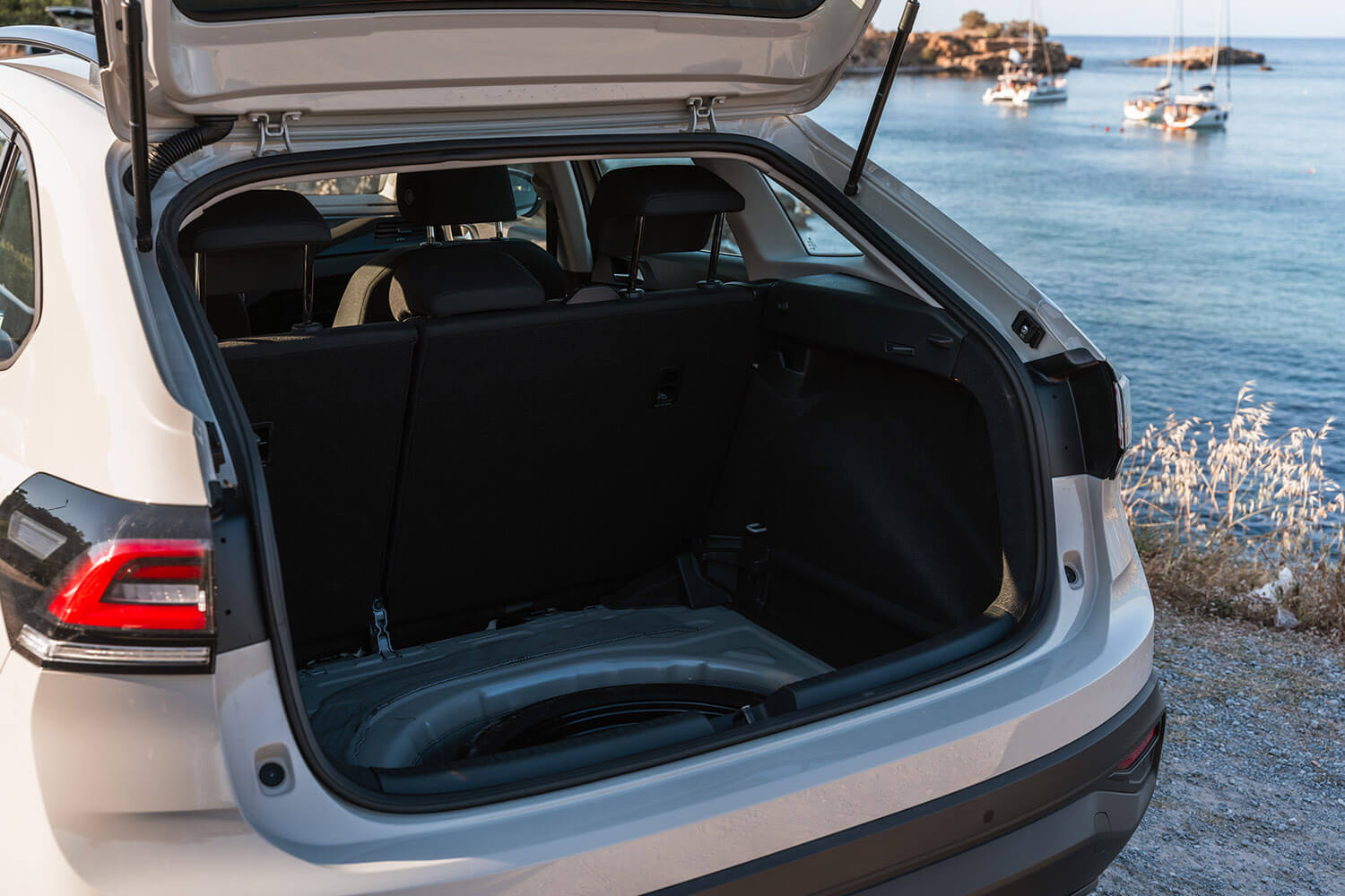 Open trunk of a white SUV by the coast, with boats visible on calm blue water in the background.