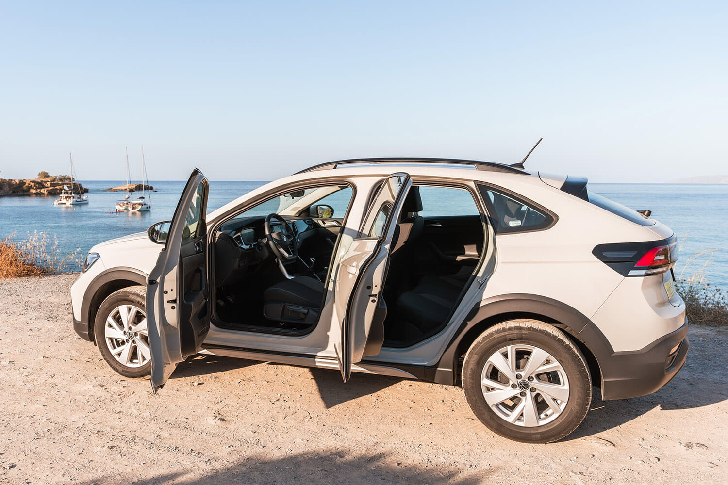 White SUV parked on a dirt road by the sea with both front and rear doors open, showing the interior and dashboard.